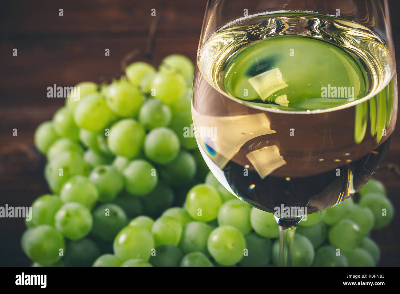 Vino bianco pieno in bicchieri di vino con un grappolo di uva verde, su uno sfondo di legno Foto Stock