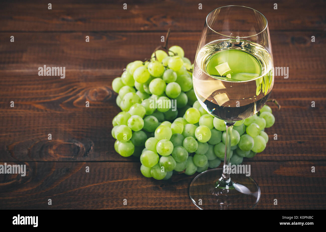 Splendido vino bianco in vetro del vino con un grappolo di uva verde, su uno sfondo di legno con spazio libero Foto Stock