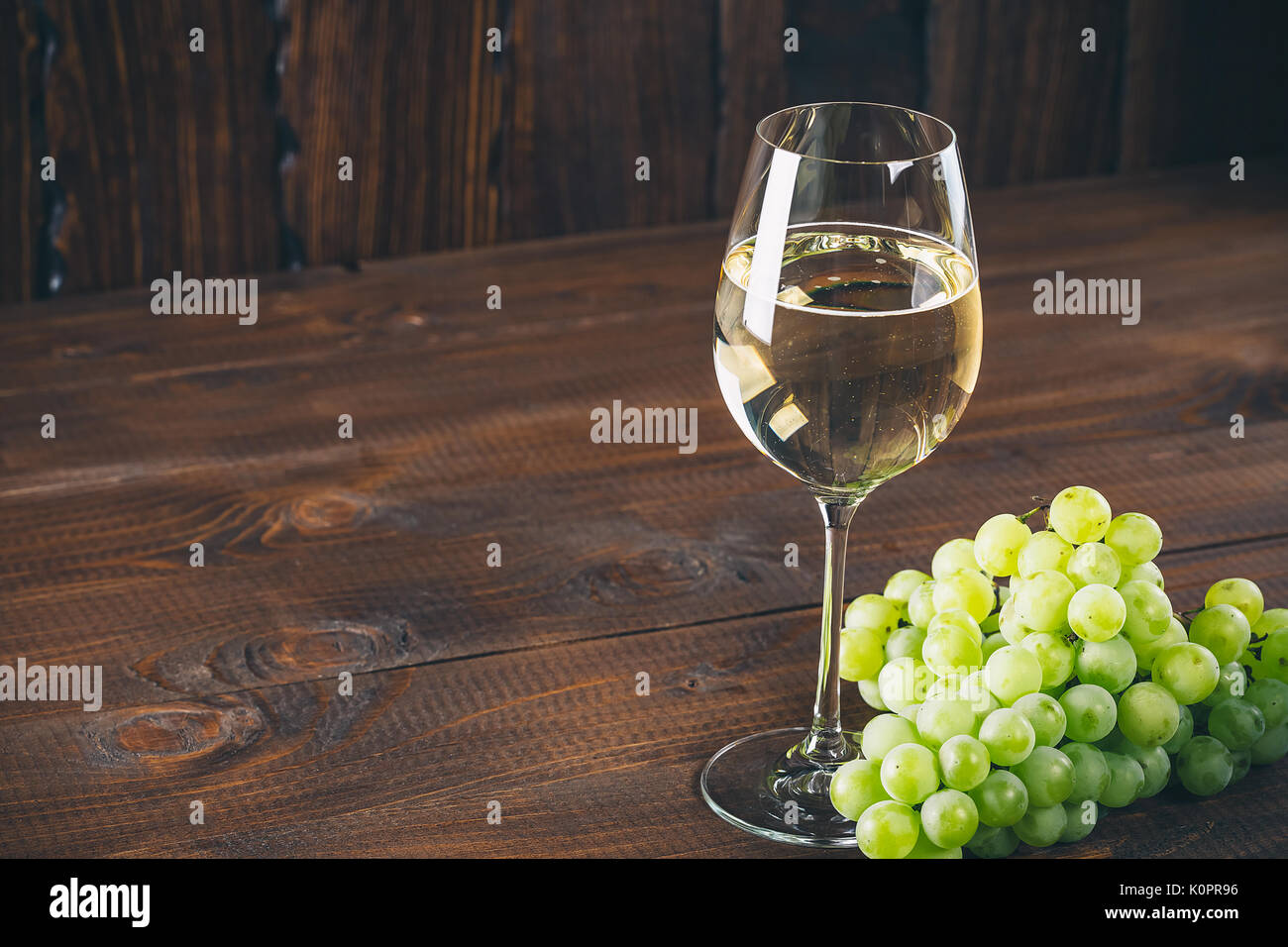 Splendido vino bianco in vetro del vino con un grappolo di uva verde, su uno sfondo di legno con spazio libero Foto Stock