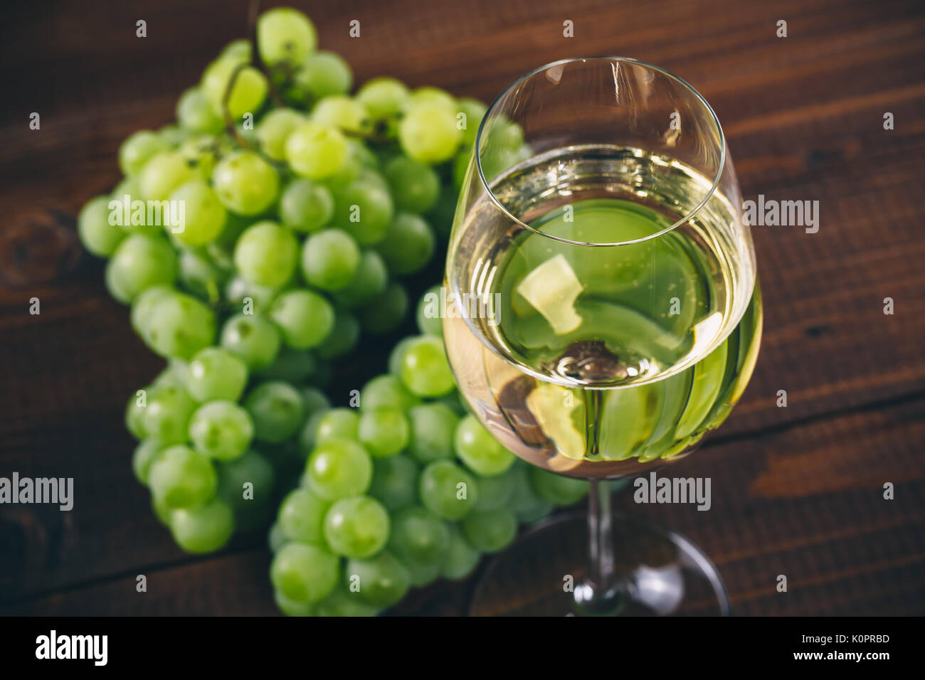 Vino bianco pieno in bicchieri di vino con un grappolo di uva verde, su uno sfondo di legno Foto Stock