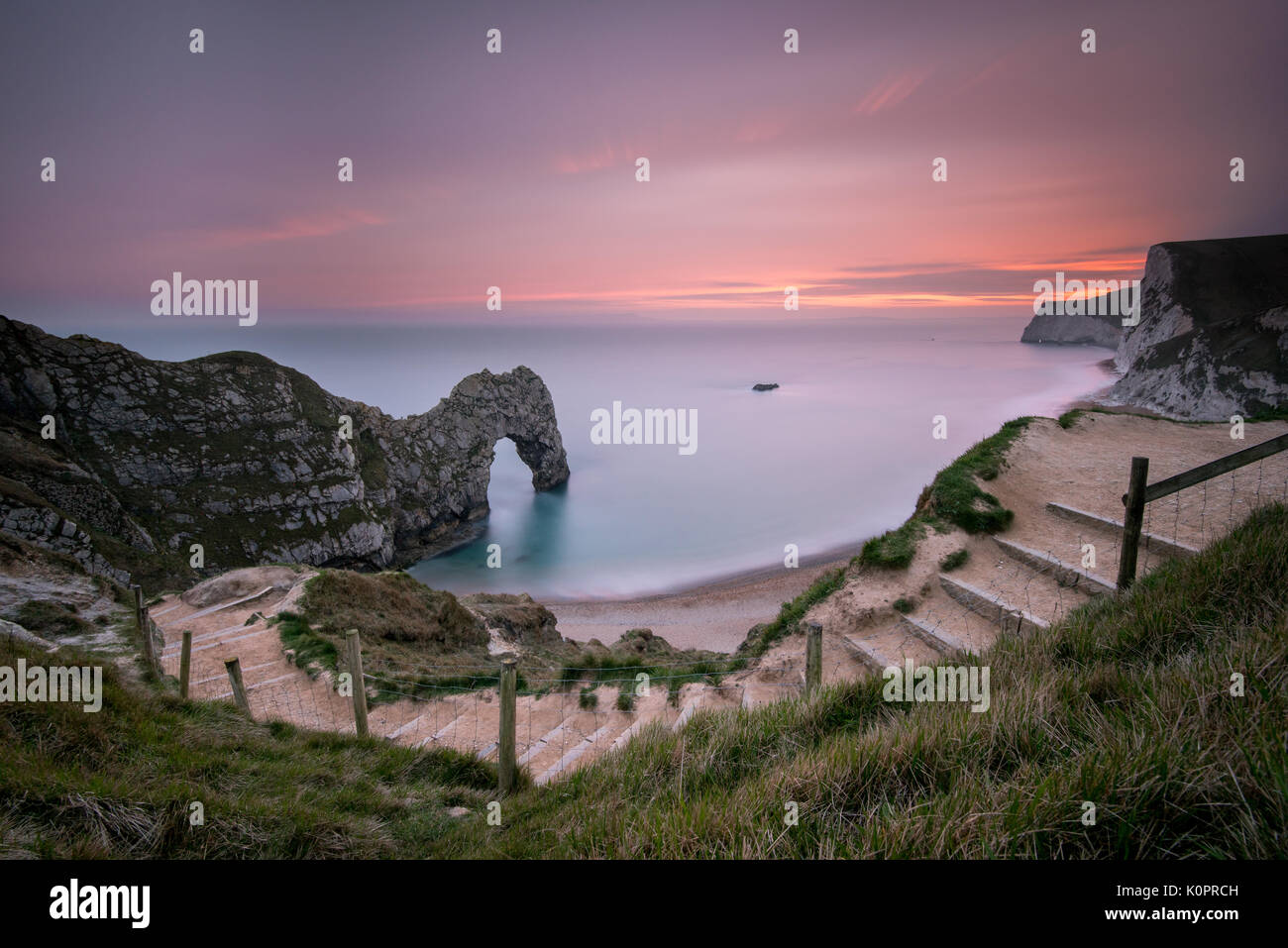 Un drammatico tramonto magenta su una serata estati a Durdle porta sul Jurassic Coast in Dorset, un sito del Patrimonio Mondiale prese con una lunga esposizione Foto Stock