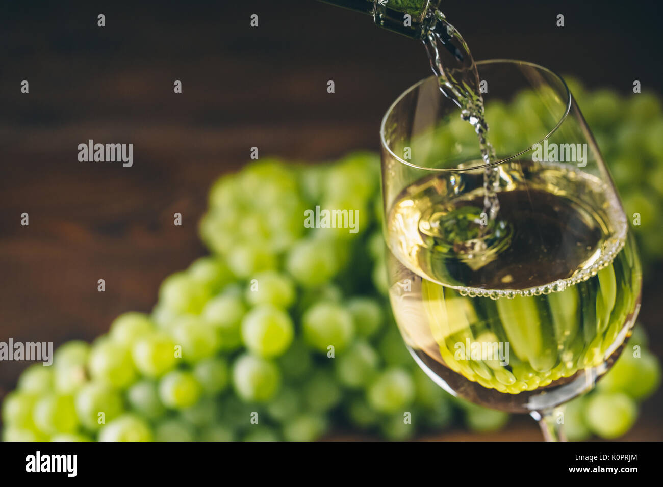 Versare il vino bianco in un bicchiere con un grappolo di uva verde contro lo sfondo di legno Foto Stock