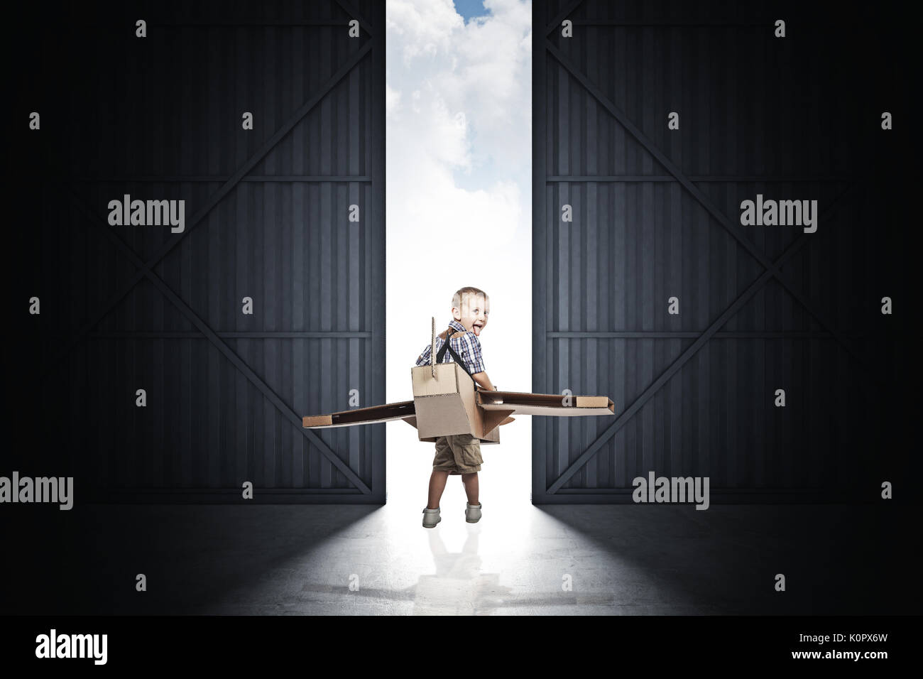 Funny bambino con aeroplano di cartone all'interno dell'hangar classico Foto Stock