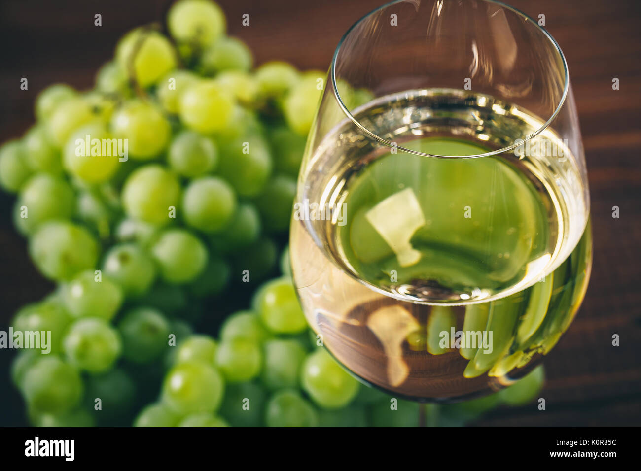 Vino bianco pieno in bicchieri di vino con un grappolo di uva verde, su uno sfondo di legno Foto Stock