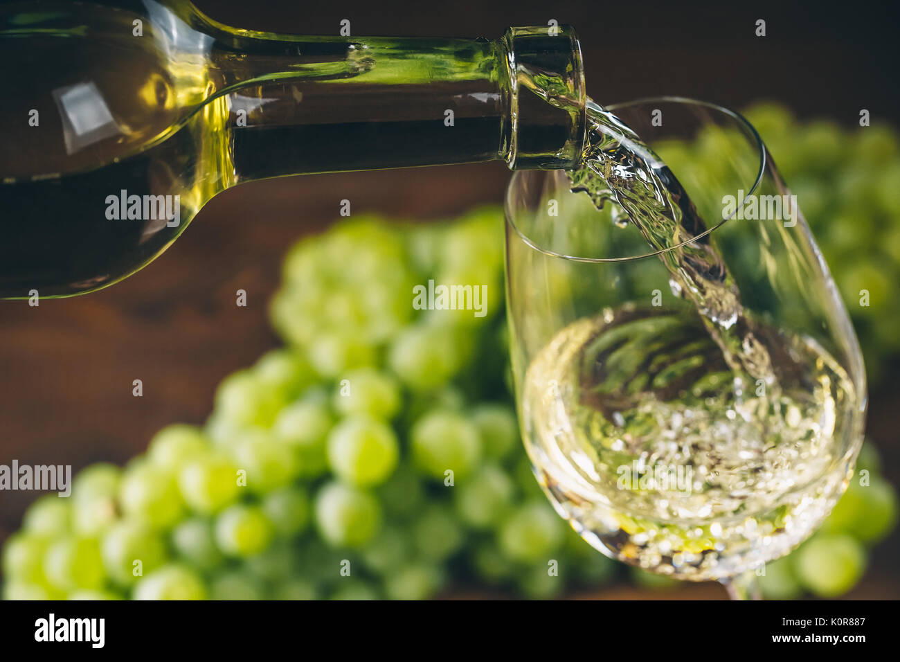 Versare il vino bianco in un bicchiere con un grappolo di uva verde contro lo sfondo di legno Foto Stock