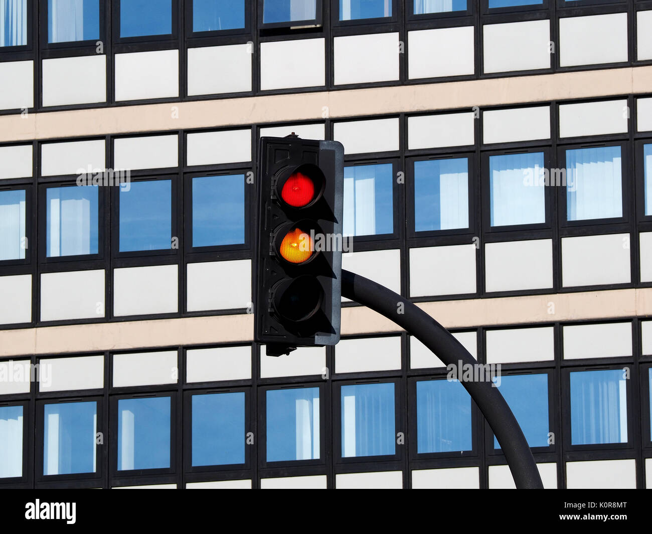 Il traffico con luce rossa e le luci color ambra brillante sullo sfondo di bianco moderno ed alto edificio di uffici con il blu del cielo si riflette in Windows Foto Stock