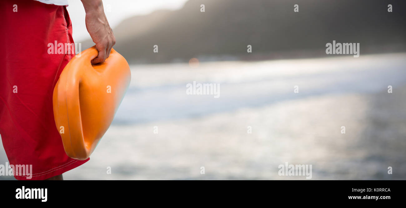 Immagine ritagliata dell'uomo azienda boa di salvataggio contro la montagna contro il cielo a spiaggia Foto Stock