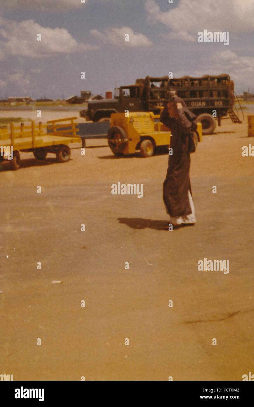 Il vietnamita uomo a camminare su di un aeroporto Aeroporto e attrezzature militari visto in background, l'unità Phu Bai Base di combattimento, Vietnam, 1964. Foto Stock