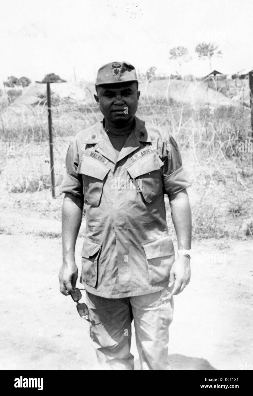 Afro-americano di esercito degli Stati Uniti il tenente al Walker in piedi nella parte anteriore del filo spinato a Phuoc Vinh Base Camp, con la prima divisione di cavalleria, durante la Guerra del Vietnam, 1964. Foto Stock