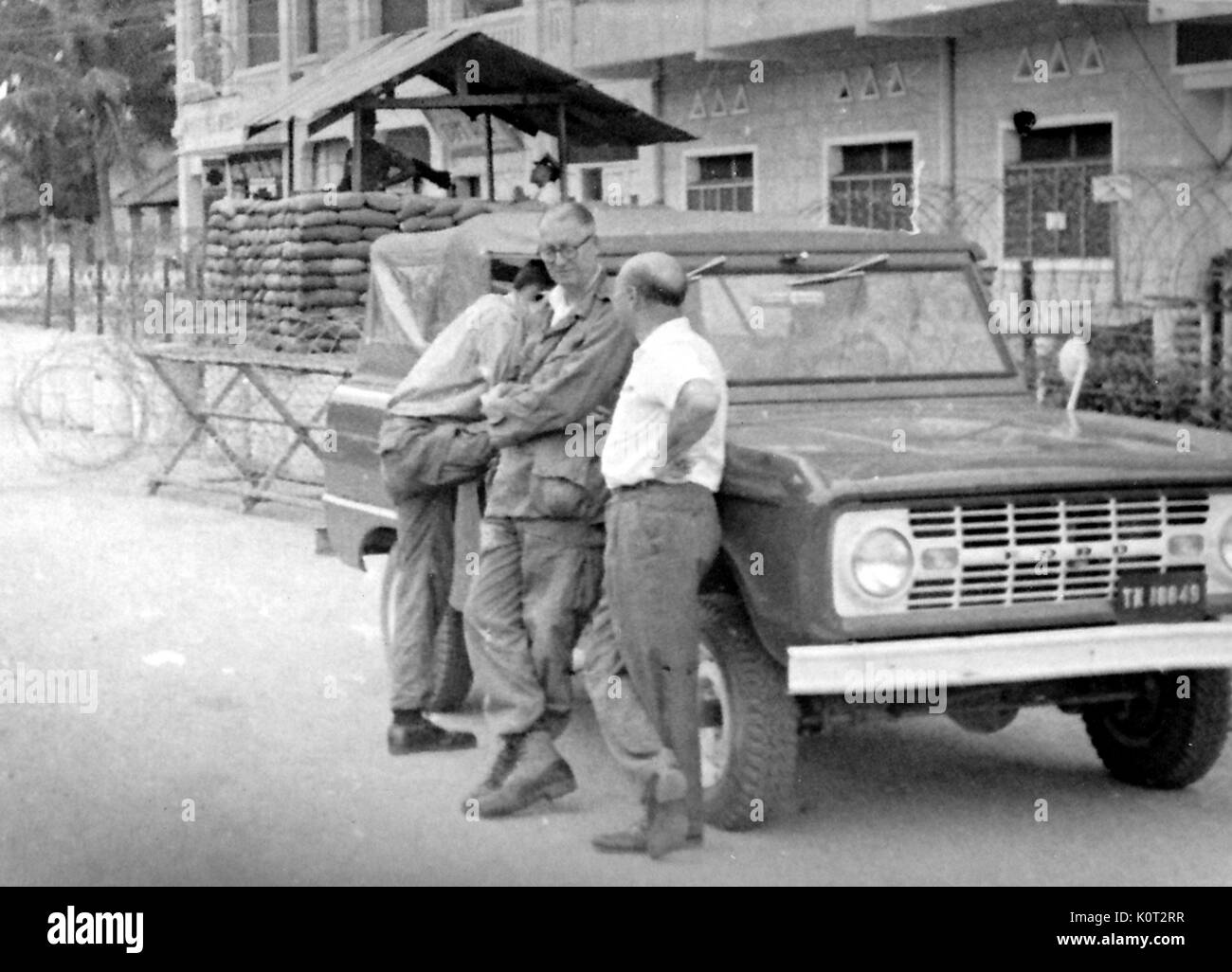 Soldati americani in piedi in un militare di check point durante la Guerra del Vietnam, poggiando su una Ford Truck, soldati con sacchi di sabbia e filo spinato a una mitragliatrice post visibili in background, 1966. Foto Stock