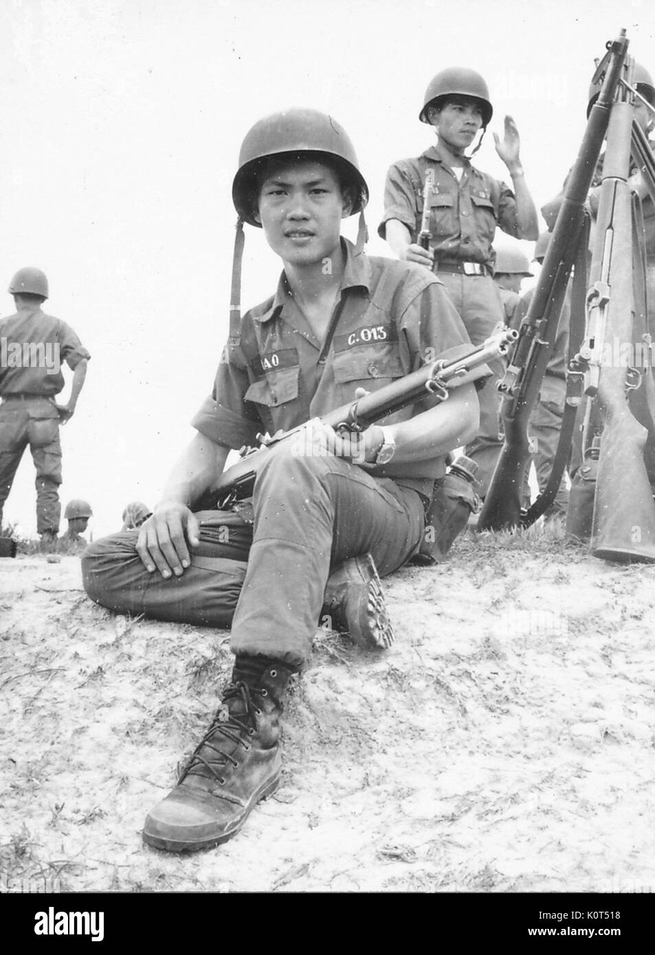 Una fotografia di un esercito della Repubblica del Vietnam soldato tenendo il suo fucile da combattimento, altri soldati sono visibili in background come pure un diversi cannoni appoggiati insieme in una posizione eretta, Vietnam, 1968. Foto Stock