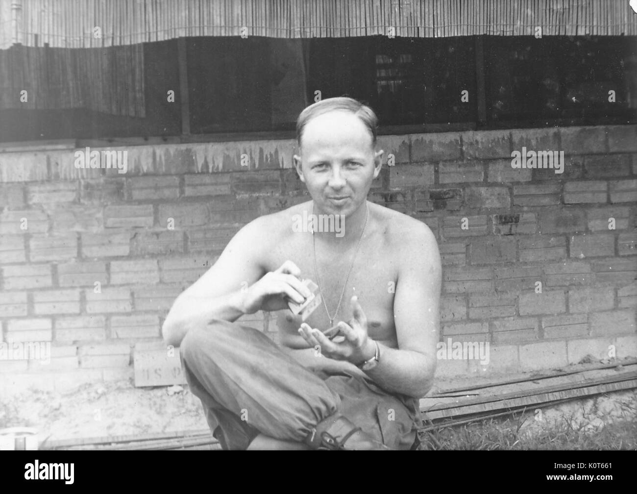 Un esercito degli Stati Uniti servizio senza una camicia su, è seduto e il molleggio giocando a carte tra le sue mani, Vietnam, 1967. Foto Stock