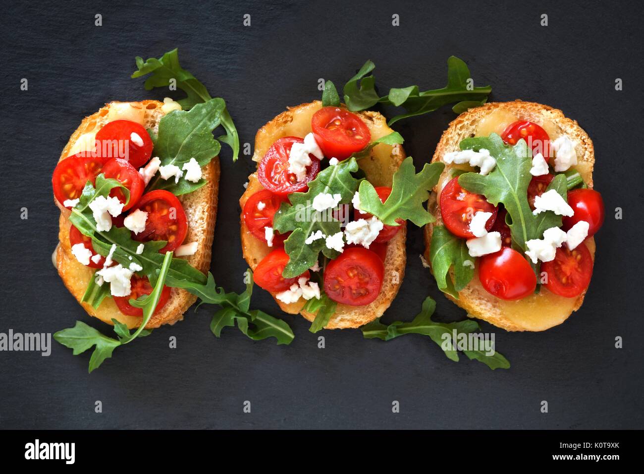 Antipasti Crostini con pomodorini, rucola e formaggio, sopra visualizza su lavagna Foto Stock