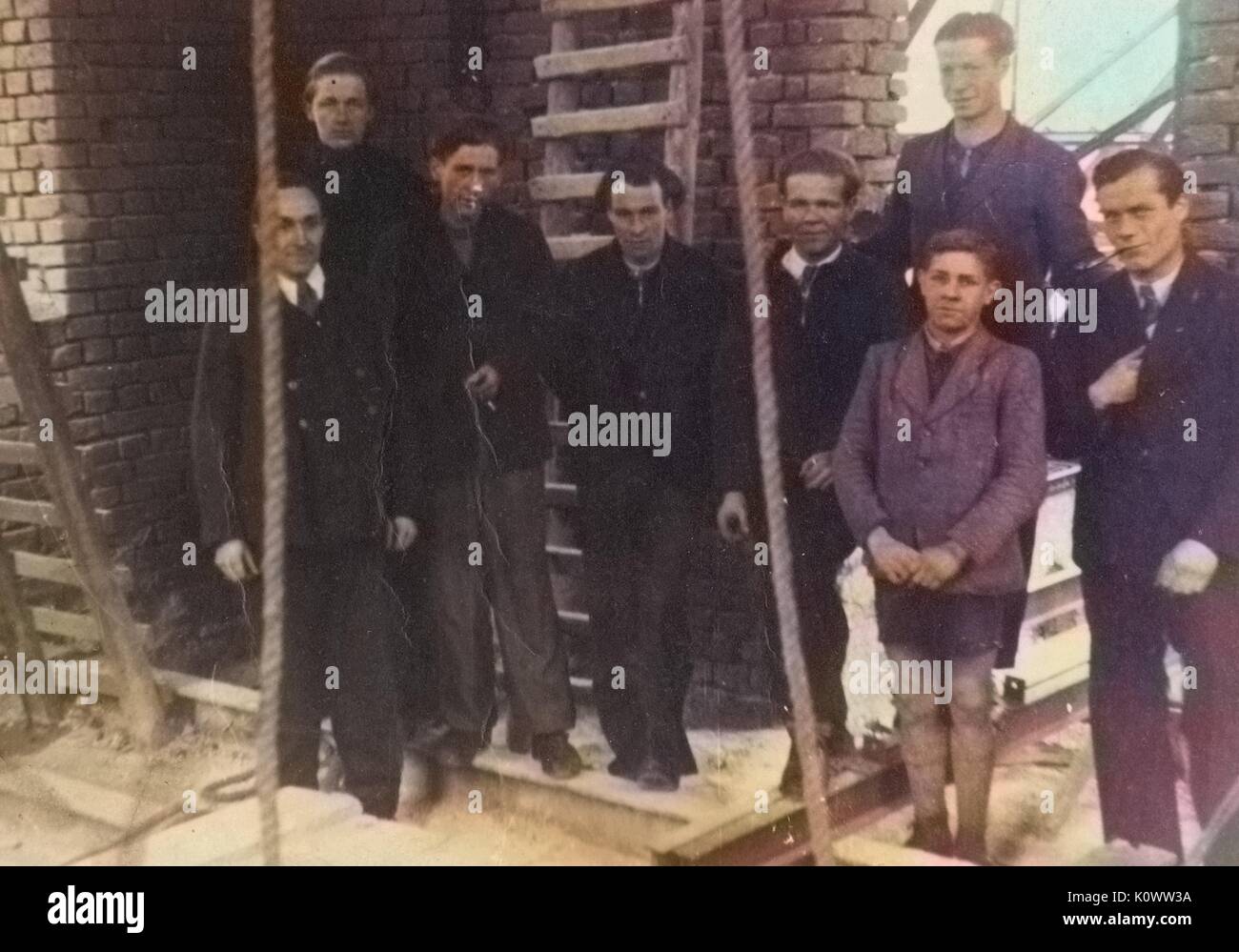 Un gruppo di uomini e ragazzi in piedi su un cantiere di fronte a un muro di mattoni, circondato da scale e corde e travi in acciaio, Germania, 1946. NOTA: l'immagine è stato colorizzato digitalmente usando un processo moderno. i colori potrebbero non essere periodo-precisa. Foto Stock