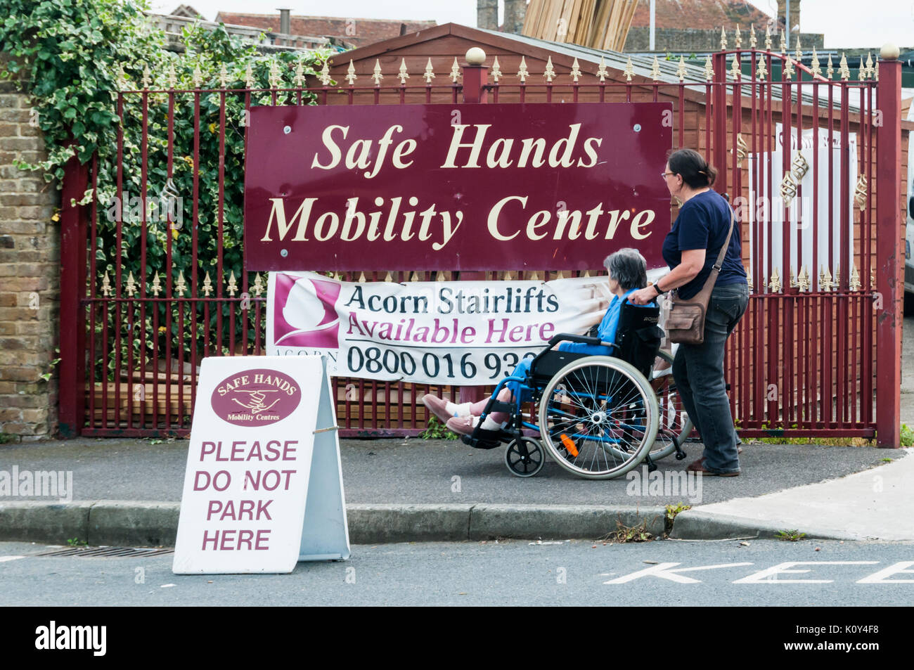 Un anziano 97 anno vecchia donna in una sedia a rotelle con il suo accompagnatore o assistente al di fuori di un mani sicure Mobility Center in Birchington, Thanet, Kent. Foto Stock