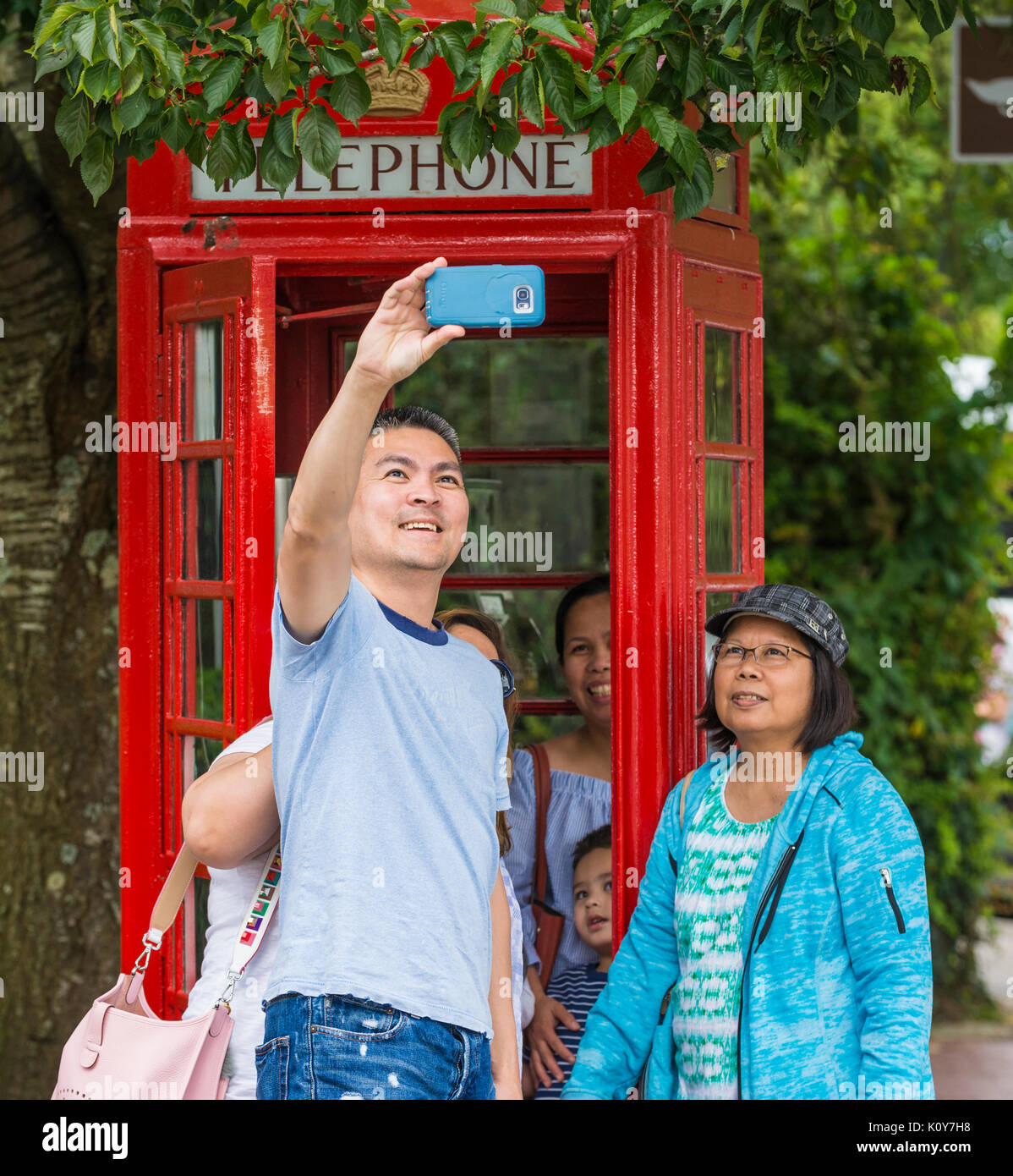 Famiglia asiatica di turisti prendendo un selfie al di fuori di un telefono rosso nella casella in Arundel, West Sussex, in Inghilterra, Regno Unito. Foto Stock