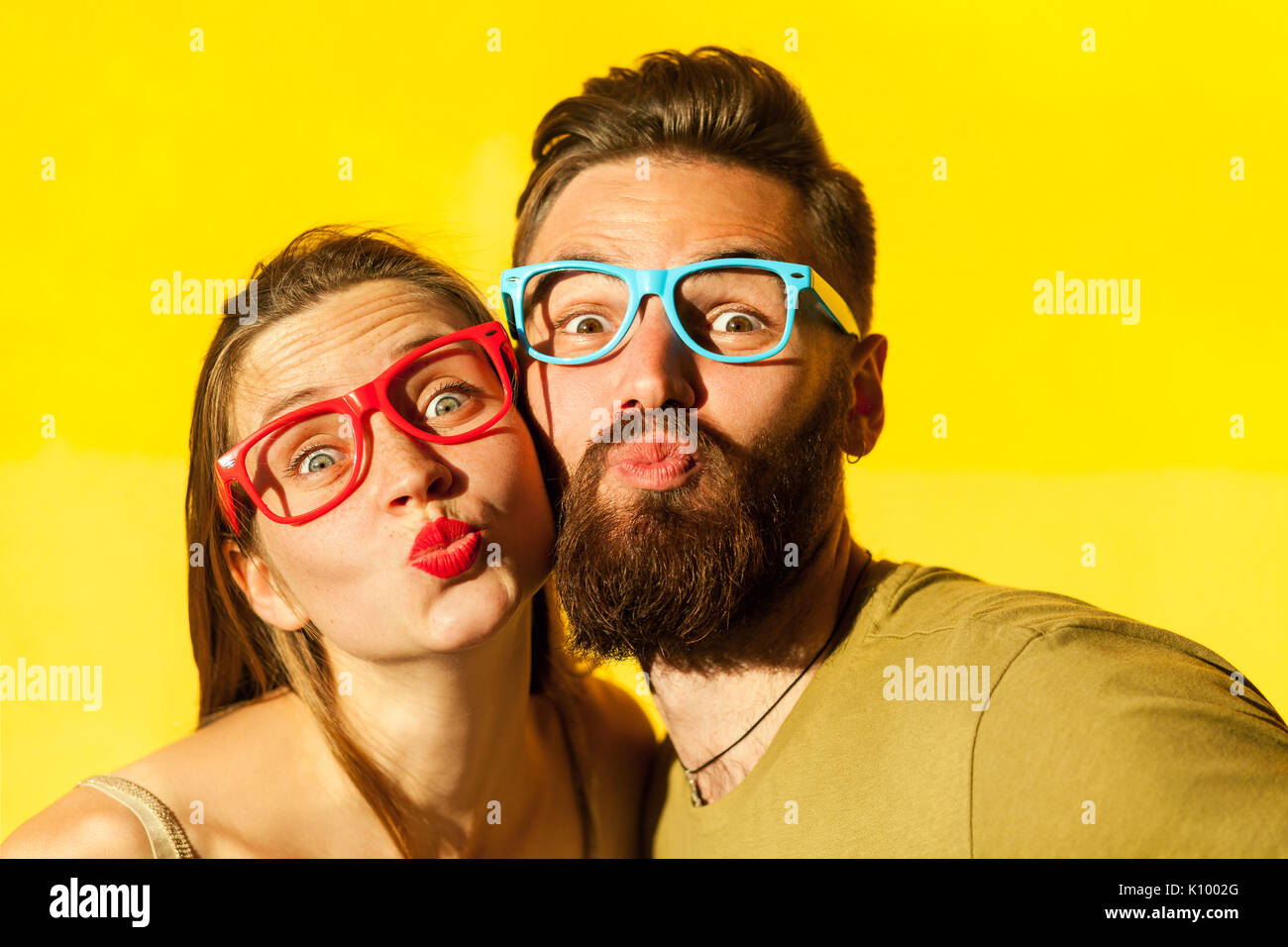 Ritratto di giovane adulto giovane con vetri di colore. Freckled donna e uomo barbuto inviare aria kissing a telecamera. Studio shot Foto Stock