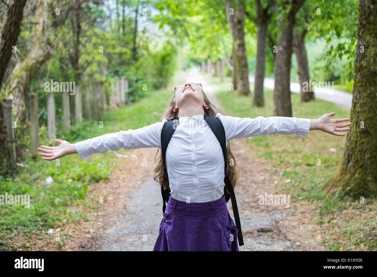 Bella bella bionda School girl bambino con occhiali, una camicia bianca e il mantello di porpora e zaino in natura alley con bracci diffusa felicemente torna t Foto Stock