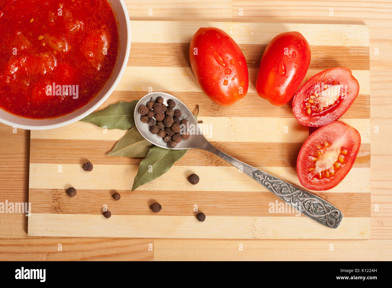 Salsa di pomodoro, pomodori freschi, la foglia di alloro e il cucchiaio con il pepe della Giamaica sulla tavola di legno, vista dall'alto. Foto Stock
