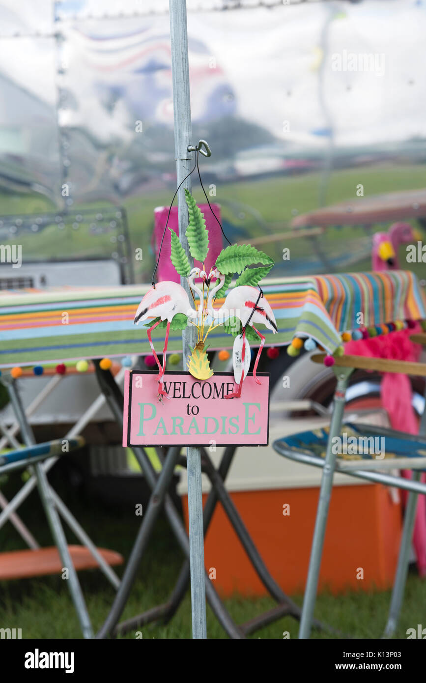 Il kitsch " Benvenuti in Paradiso' camping segno davanti a un americano roulotte Airstream a un vintage retrò festival. Regno Unito Foto Stock