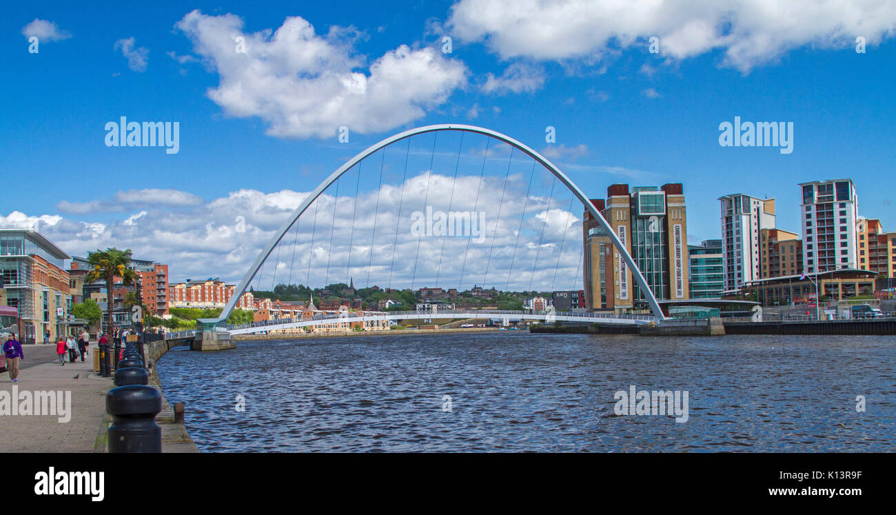 Vista panoramica di Gateshead Millennium Bridge, di ribaltamento del ponte pedonale di fronte fiume Tyne a Newcastle-upon-Tyne con edifici della città sotto il cielo blu Foto Stock