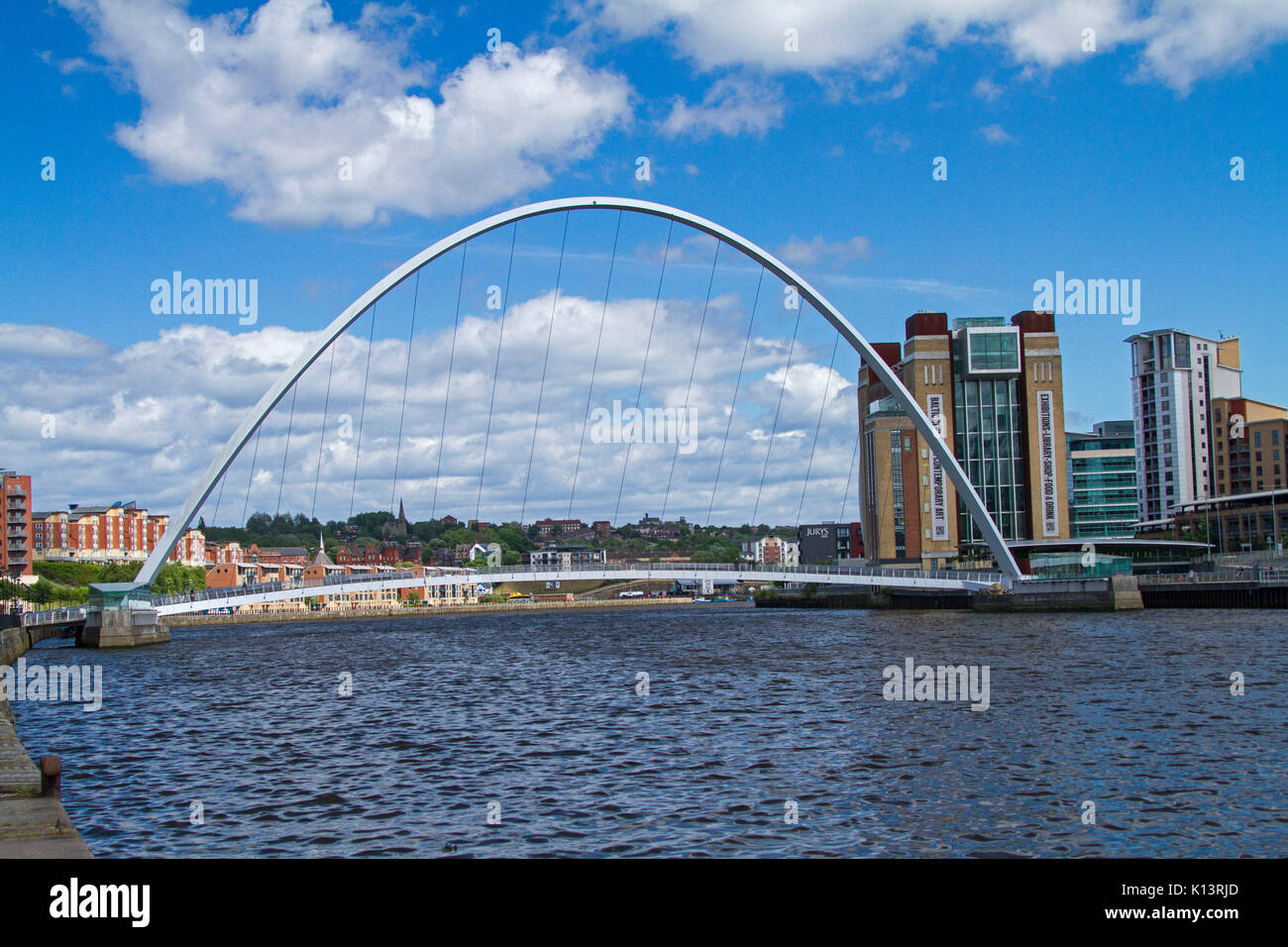 Gateshead Millennium Bridge, di ribaltamento del ponte pedonale di fronte fiume Tyne a Newcastle-upon-Tyne con edifici della città nelle vicinanze sotto il cielo blu Foto Stock