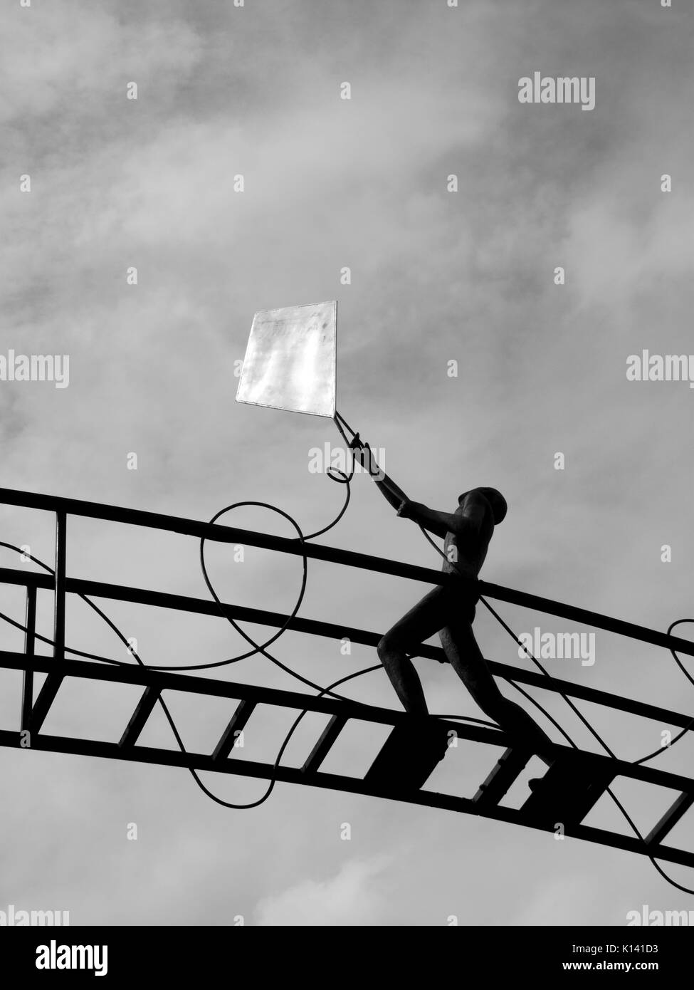 Punto di riferimento della città di una figura di bronzo di un ragazzino volare un aquilone dorato mentre passeggiate attraverso un ponte al di sopra di pergamena Street Foto Stock