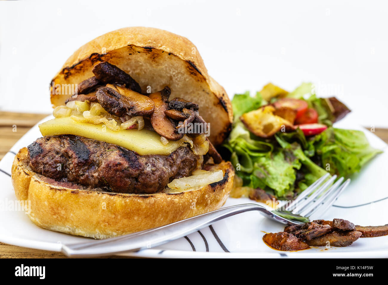 Succose grigliate di hamburger che è coperto in fuso Gruyère formaggi, funghi saltati e caramellare le cipolle. Un lato insalata di verdure fresche, pomodoro, e Foto Stock