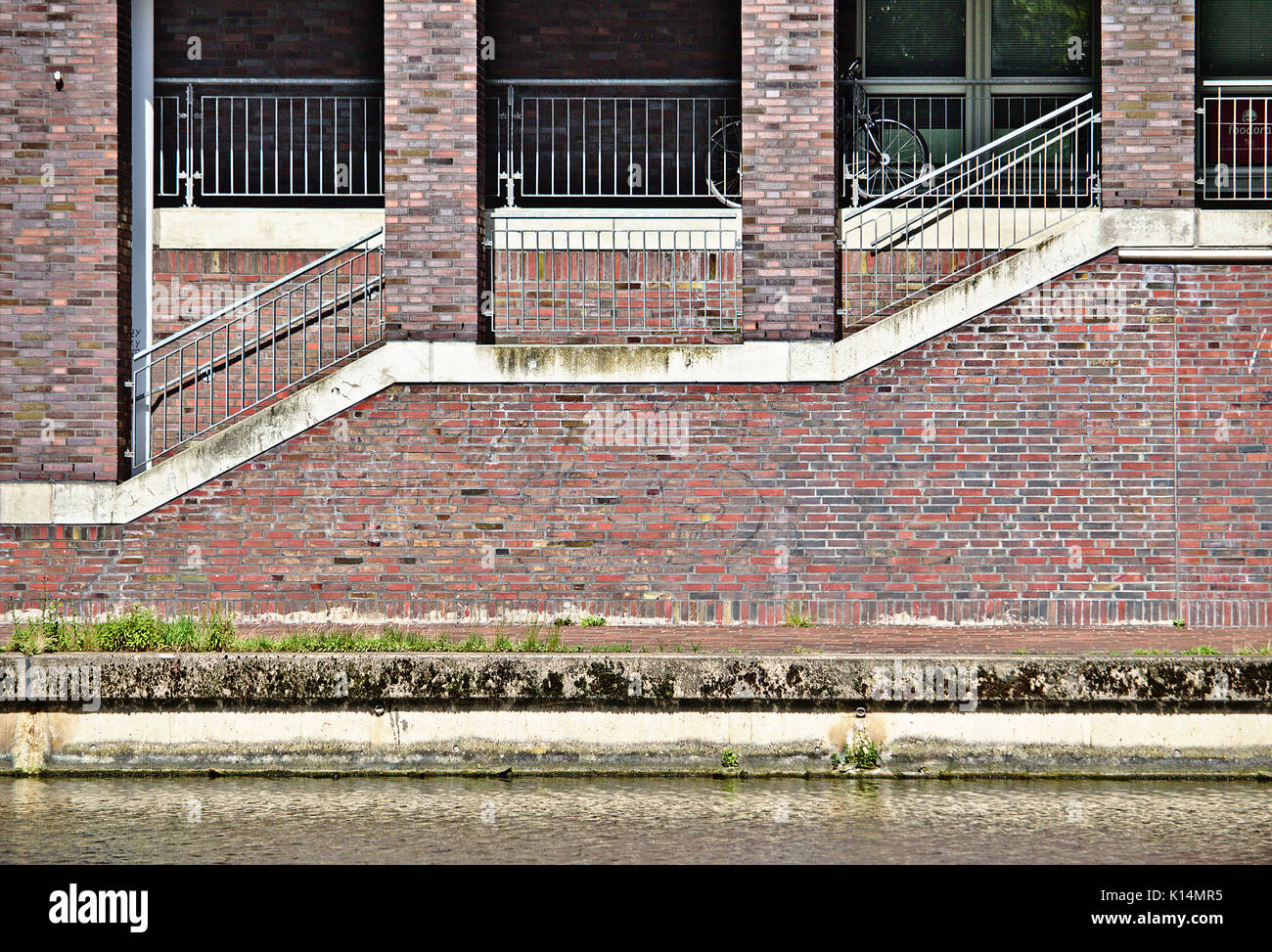 Edificio sul lungomare con il marciapiede, rampa di scale, rosso e grigio muro di mattoni e pilastri in mattoni Foto Stock