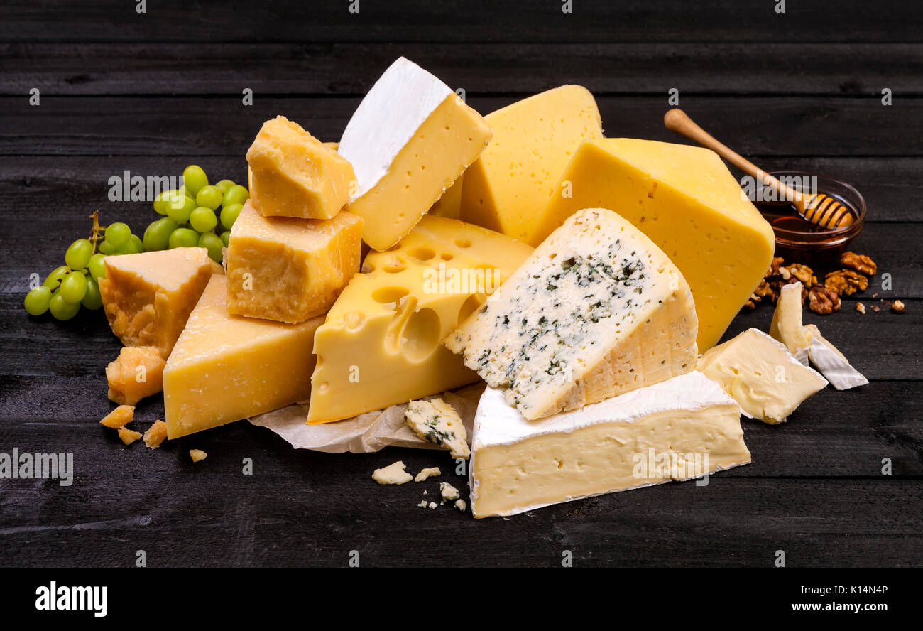 Vari tipi di formaggio su tavoli in legno nero. Foto Stock