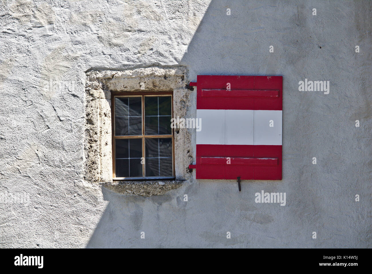Intonacate ruvido muro di castello con finestra e persiane di legno colorato come la bandiera austriaca, in parte ombreggiato e parzialmente illuminata da luce solare Foto Stock