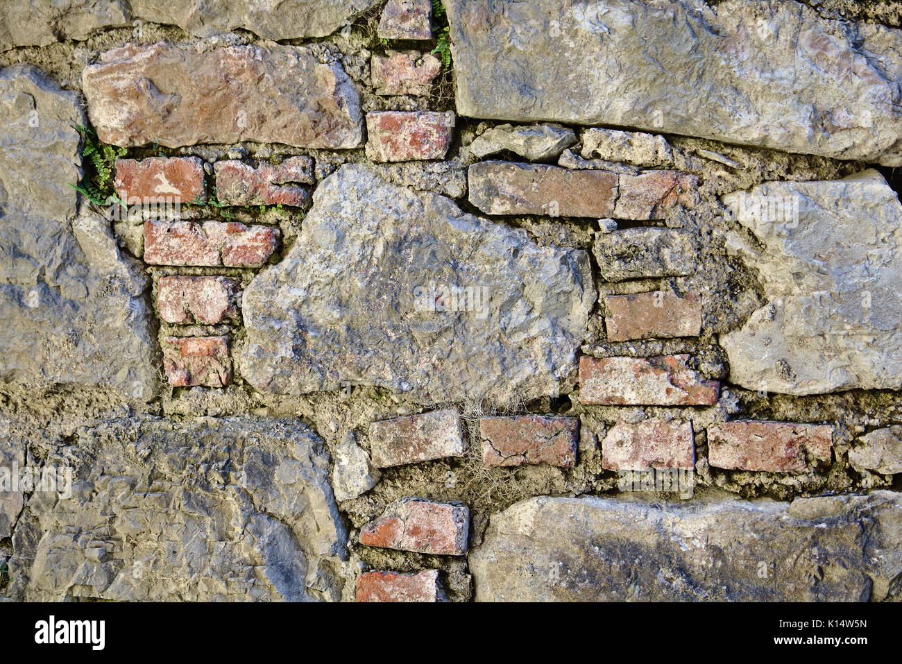 Antico castello muro fatto di mattoni rossi e grandi pietre di campo con mortaio di frantumazione Foto Stock