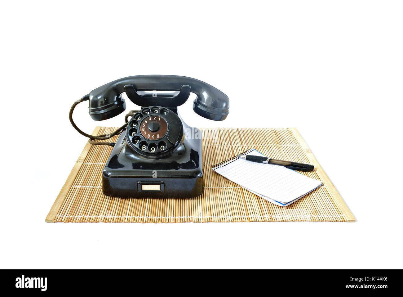 Vintage telefono sul tappetino di rattan con la penna nera e blocco note con copyspace isolato su sfondo bianco Foto Stock