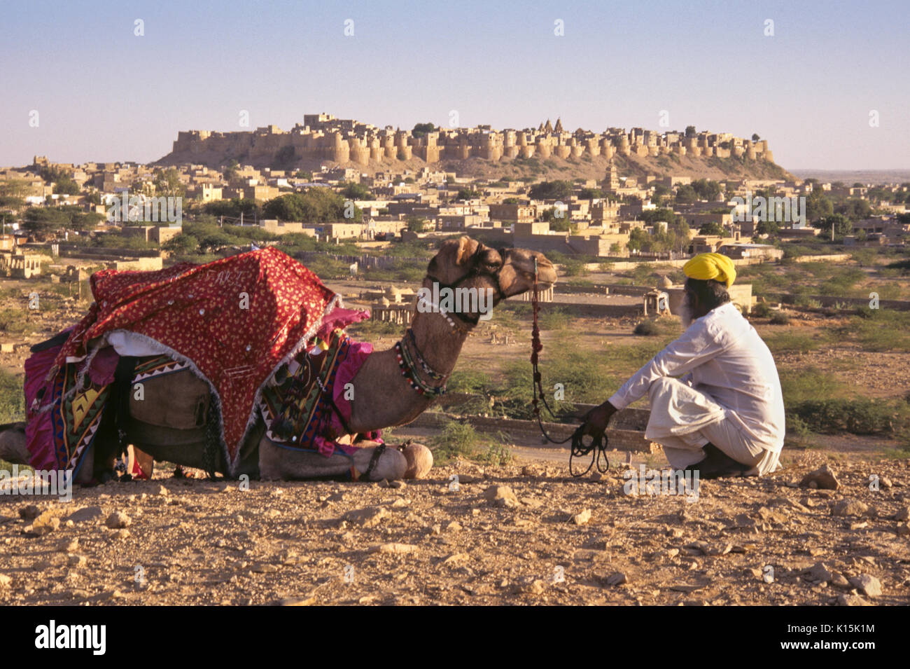 Uomo con il cammello, Jaisalmer Fort in distanza, Jaisalmer, Rajasthan, India Foto Stock