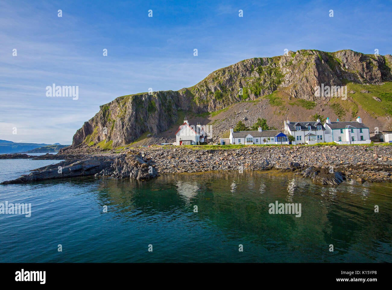 Splendida vista del villaggio di Ellenabeich / Easdale, Seil Isola, Scozia, con casette bianche alla base della scogliera di roccia si riflette nelle calme acque dell'oceano Foto Stock