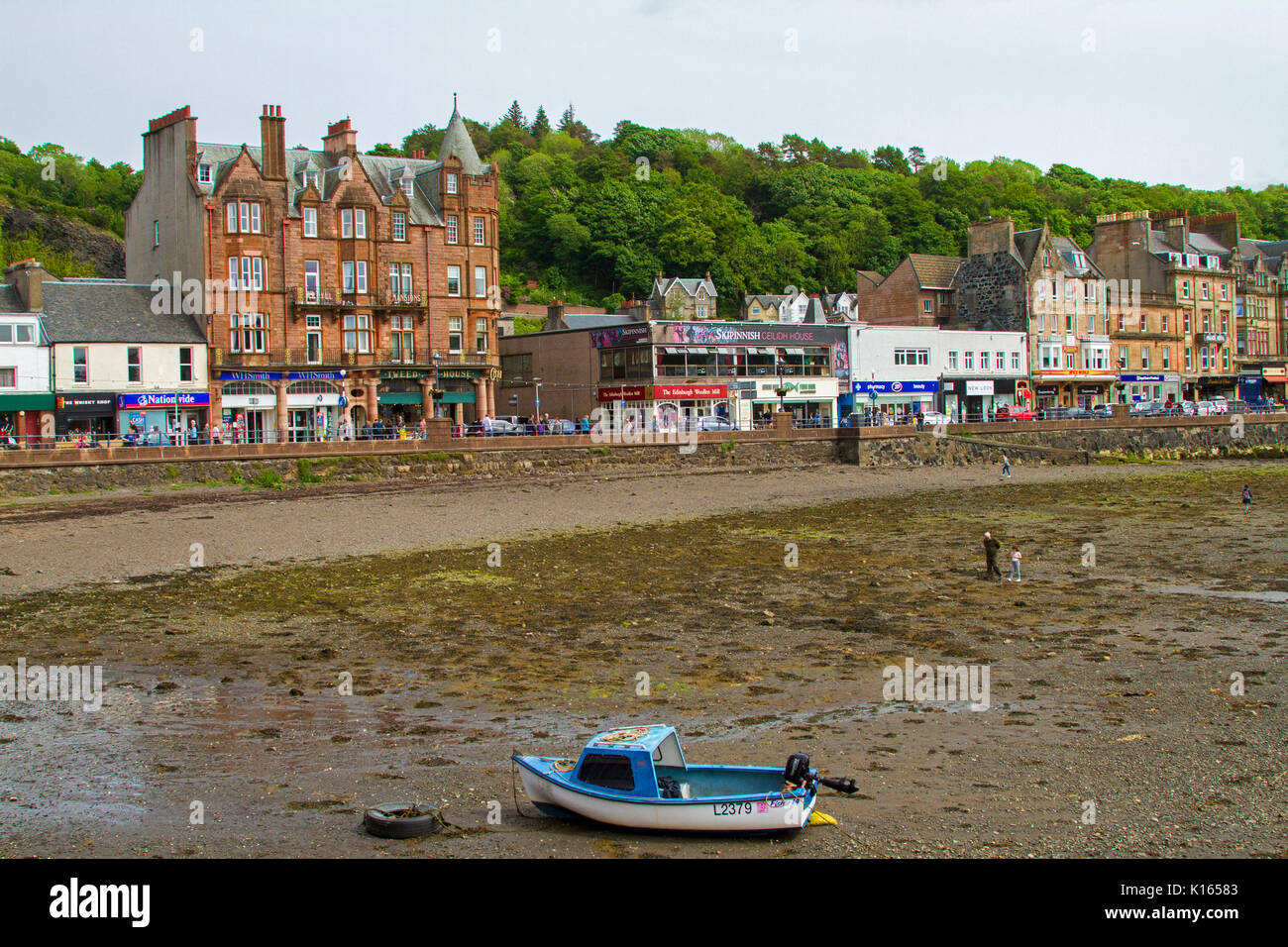Cittadina Scozzese di Oban con fila di edifici fronte mare con barca in porto a bassa marea in primo piano Foto Stock