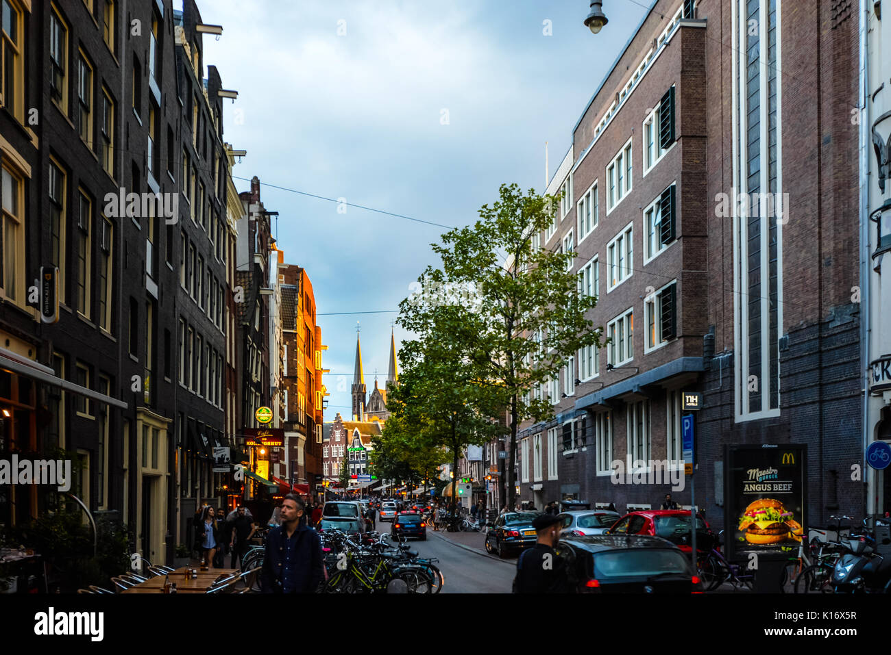 Di sera presto come il sole scende nel centro storico di Amsterdam con una grande chiesa con le sue guglie in background Foto Stock