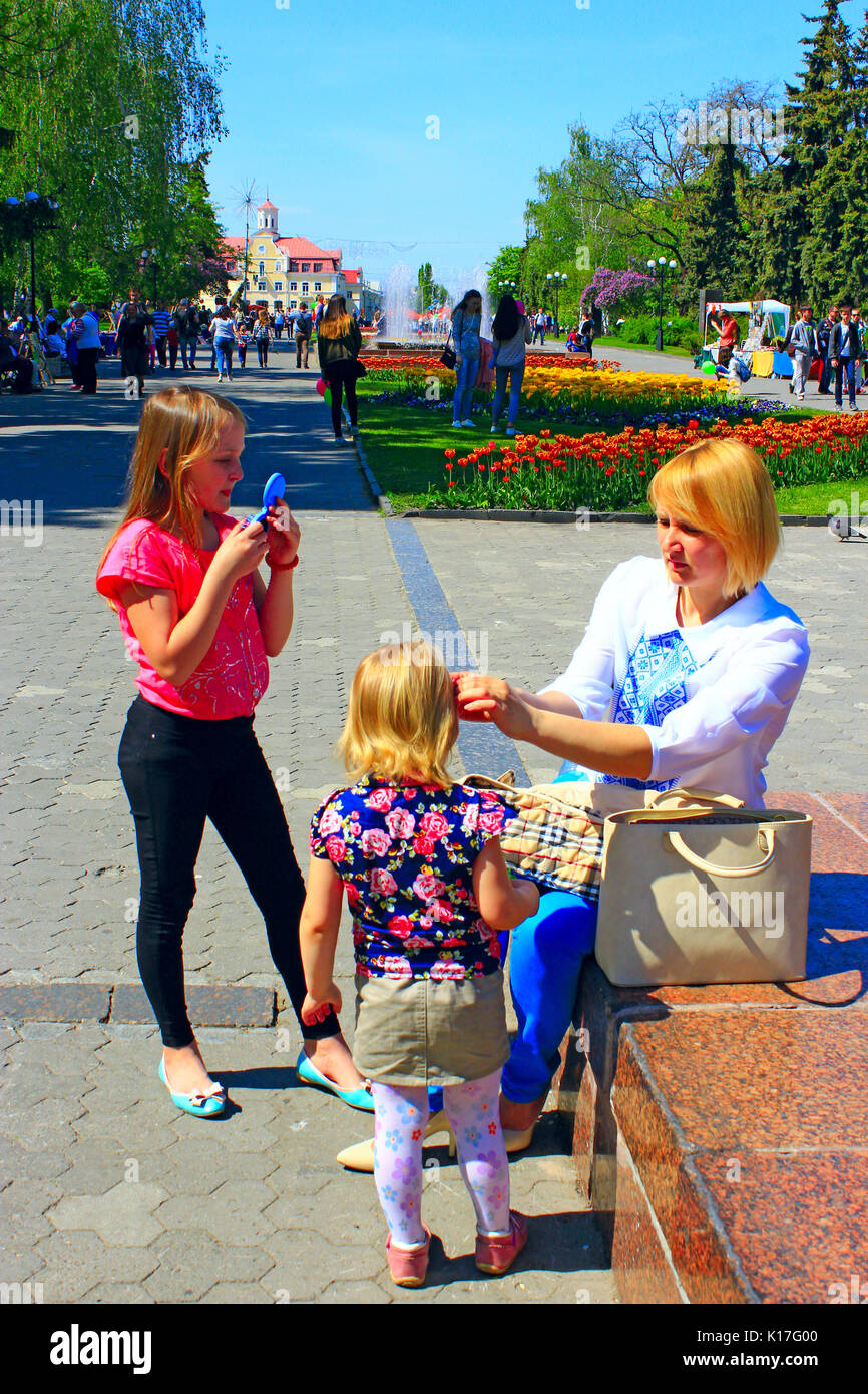 Madre corregge la figlia della capelli durante una passeggiata attraverso la città di primavera. Famiglia a piedi attraverso la città di primavera Foto Stock