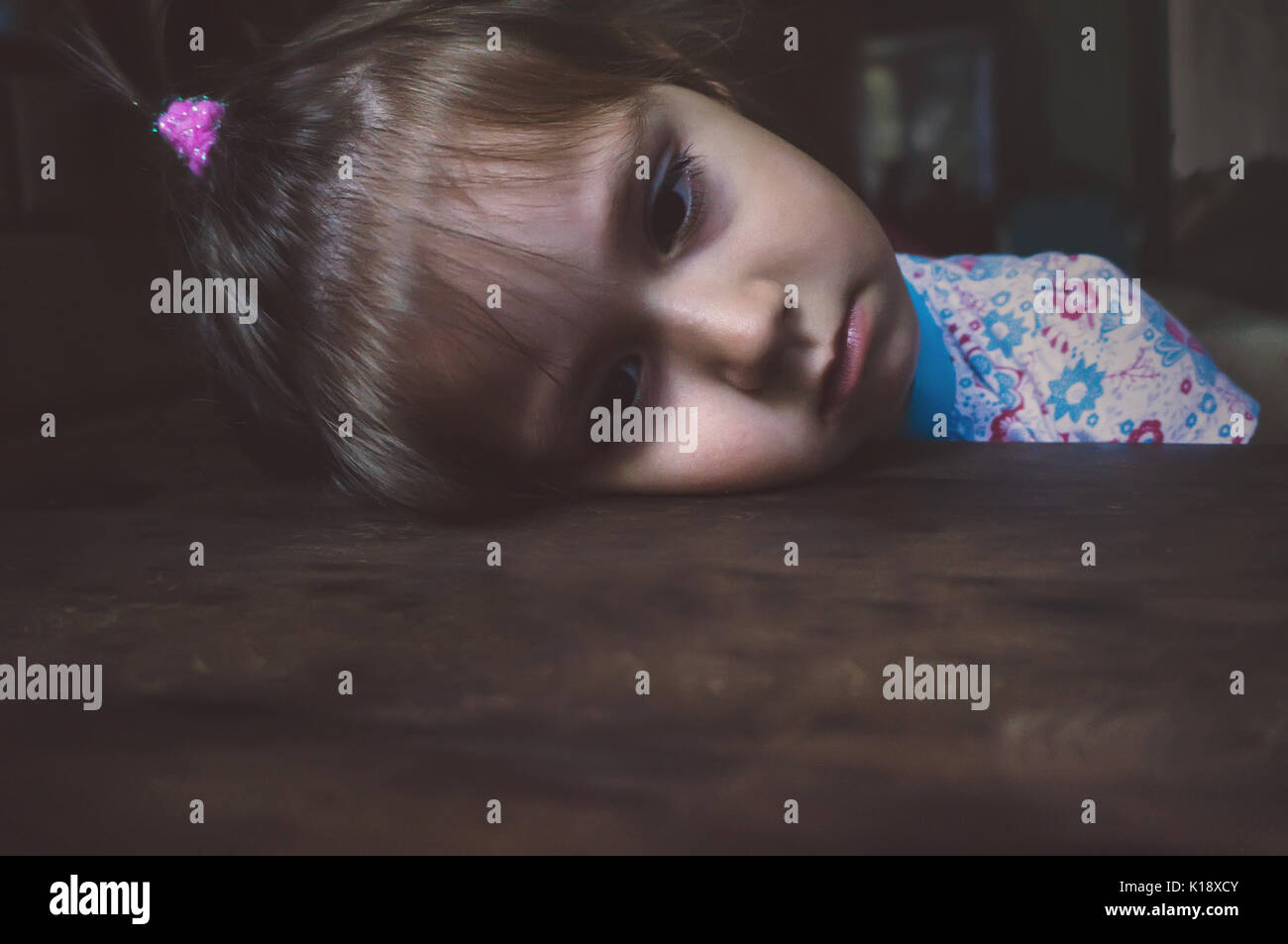 Ritratto di triste bambina. ragazza piegò la sua testa sul tavolo e guarda verso il basso prima di lui. La faccia triste. Il bambino stanco risiede con la sua testa su un di legno tabl Foto Stock