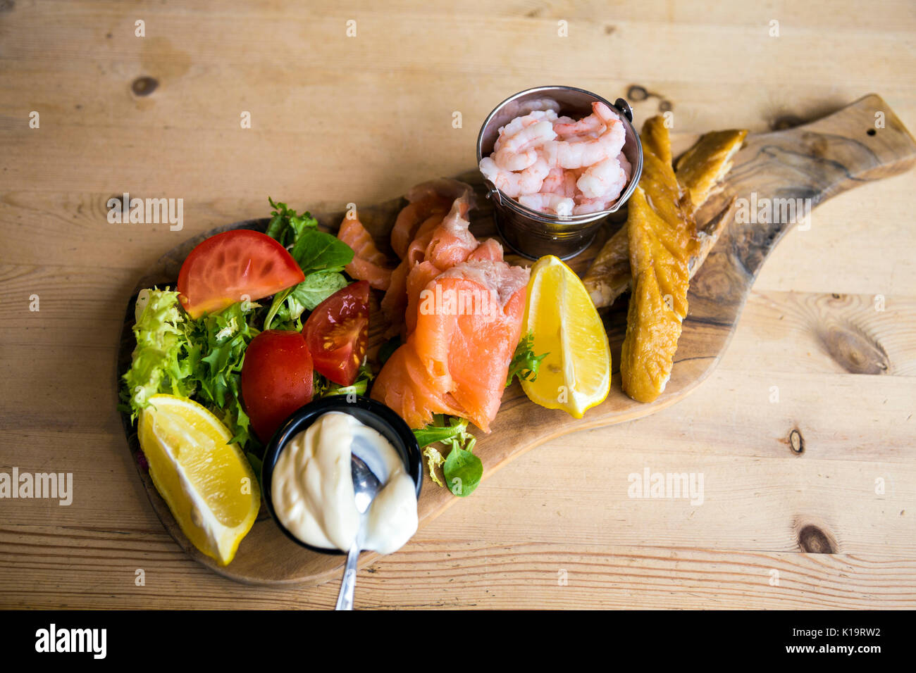 Piatto di frutti di mare su di un tagliere di legno e un tavolo di legno, gamberi, sgombro, salmone affumicato, insalata Foto Stock