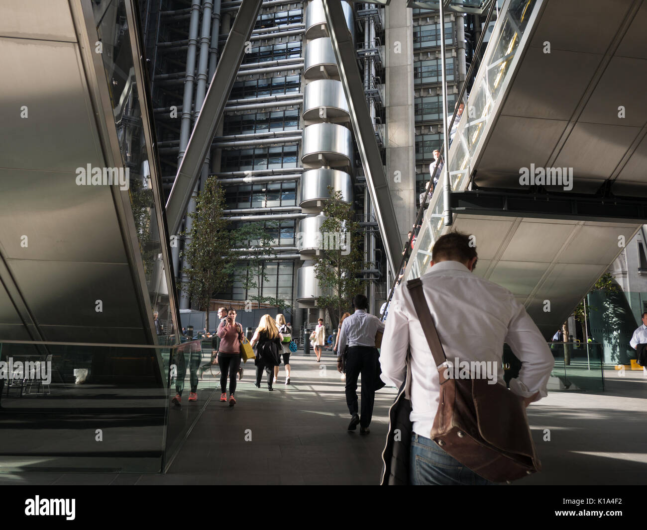 Lloyds di Londra visto da tra le scale mobili dell'edificio Leadenhall, con i lavoratori della città che passano attraverso la passerella Foto Stock