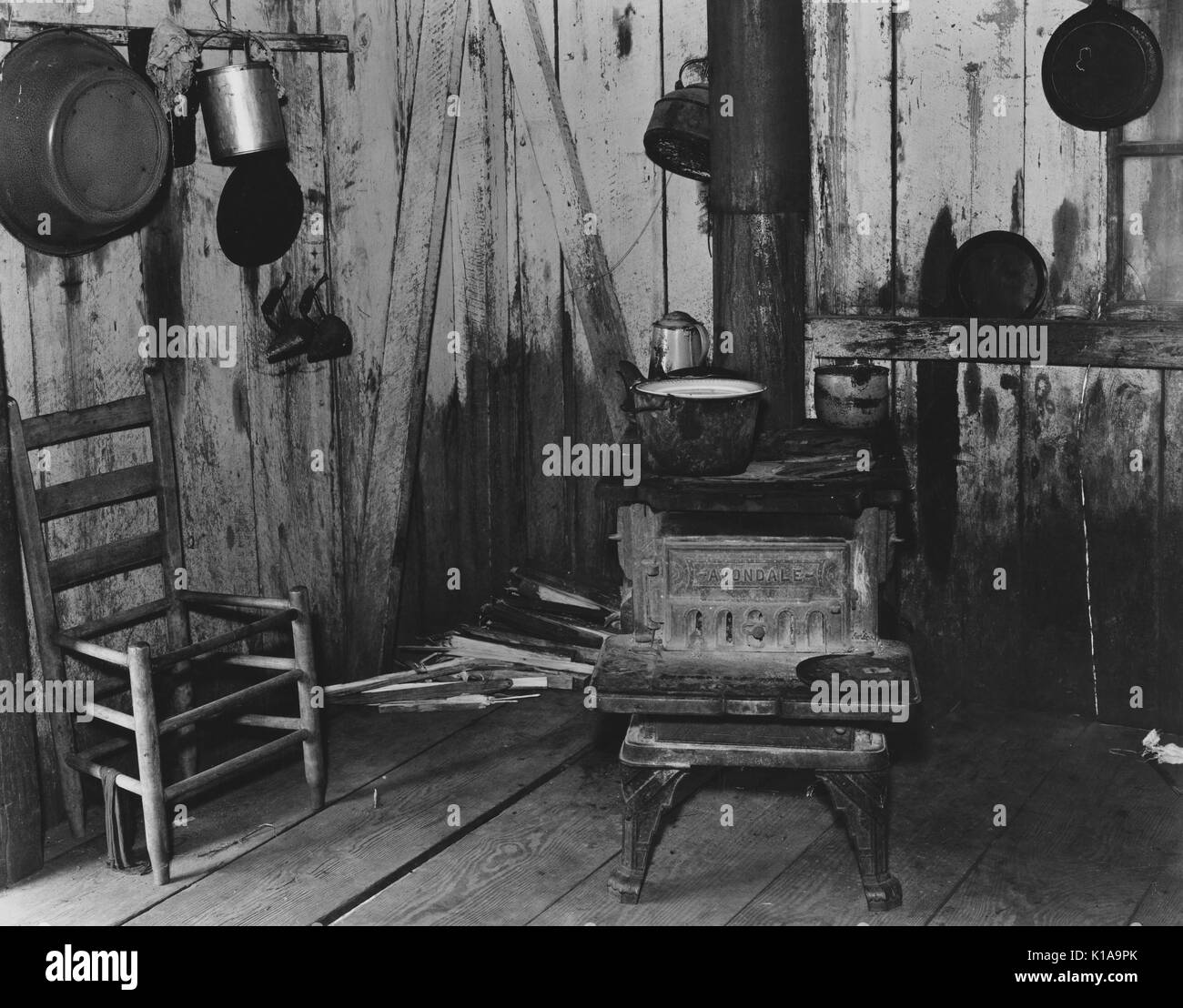 Una modesta cucina appartenenti ad un mezzadri, con un buon uso di stufa di legno, una sedia in attesa di riparazione contro la parete e pentole e bollitori appesi ai muri, Hale County, Alabama, 1936. Dalla Biblioteca Pubblica di New York. Foto Stock