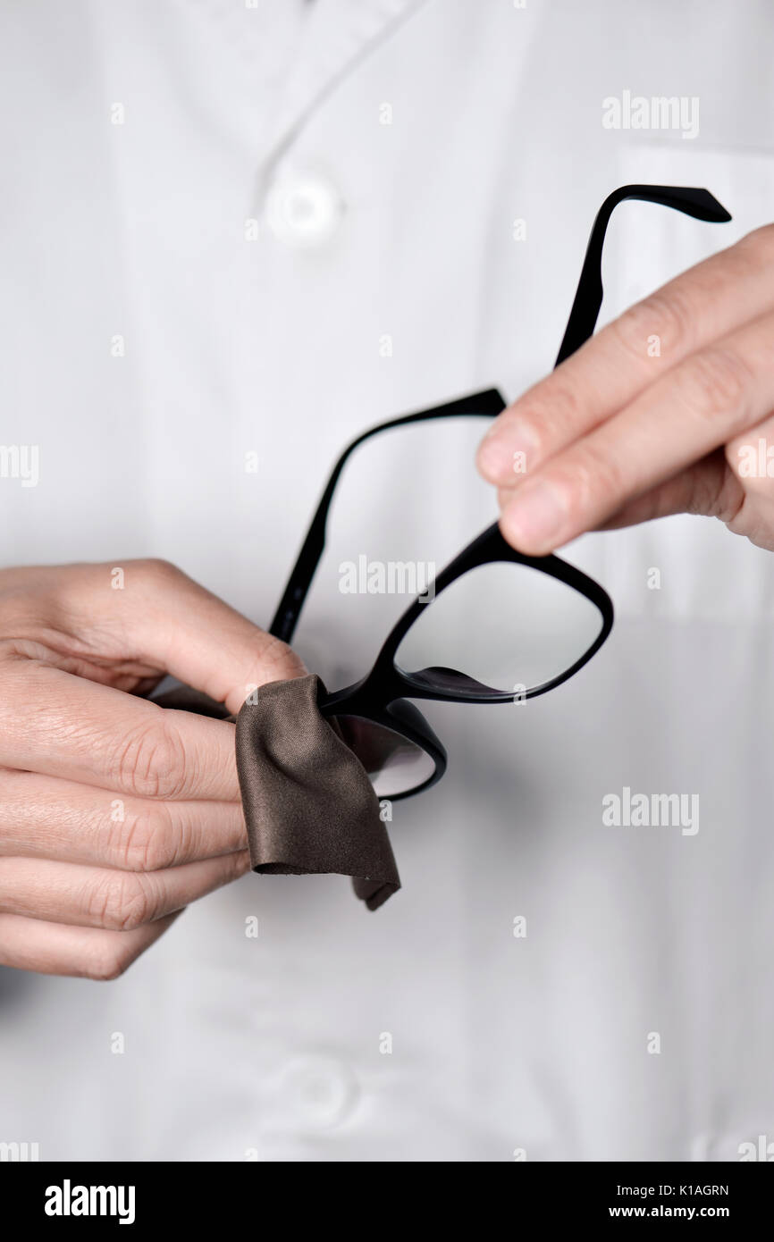 Primo piano di un giovane uomo ottico in un manto bianco pulizia delle lenti di un paio di occhiali con un panno in microfibra Foto Stock