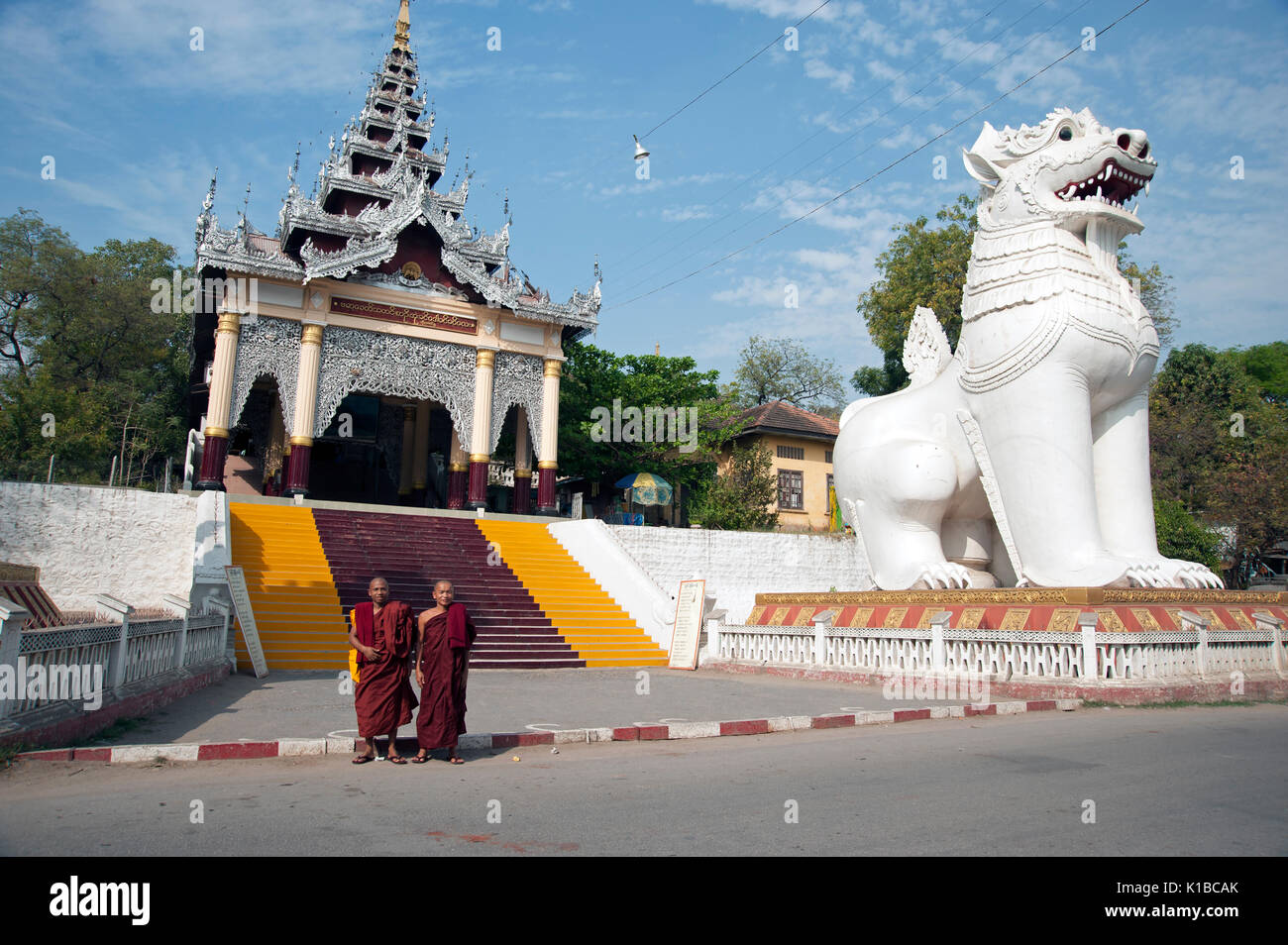 Due monaci buddisti posano per una fotografia ai piedi della scalinata che conduce al Mandalay Hill Myanmar davanti a un enorme statua Chinte Foto Stock