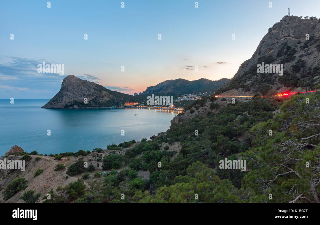 Vista della baia al villaggio vicino alle montagne e con un grande promontorio al mare al tramonto. La traccia di luce di passare attraverso le serp Foto Stock
