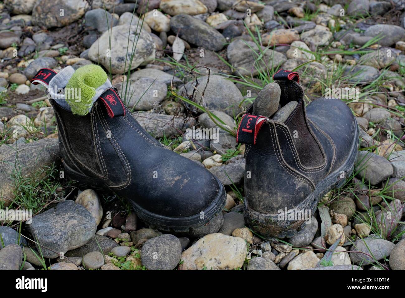 Una sporca coppia di bambino redback stivali da lavoro, abbandonato sul terreno pietroso. Foto Stock