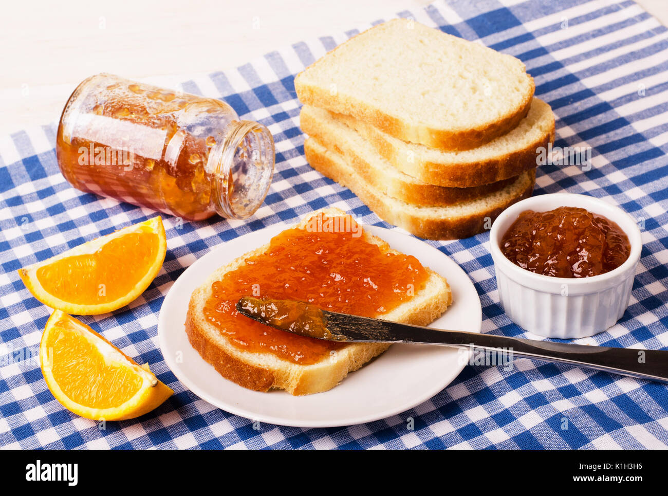 Un vasetto di marmellata di arancio con il pane su scacchi tovaglia blu, primo piano Foto Stock