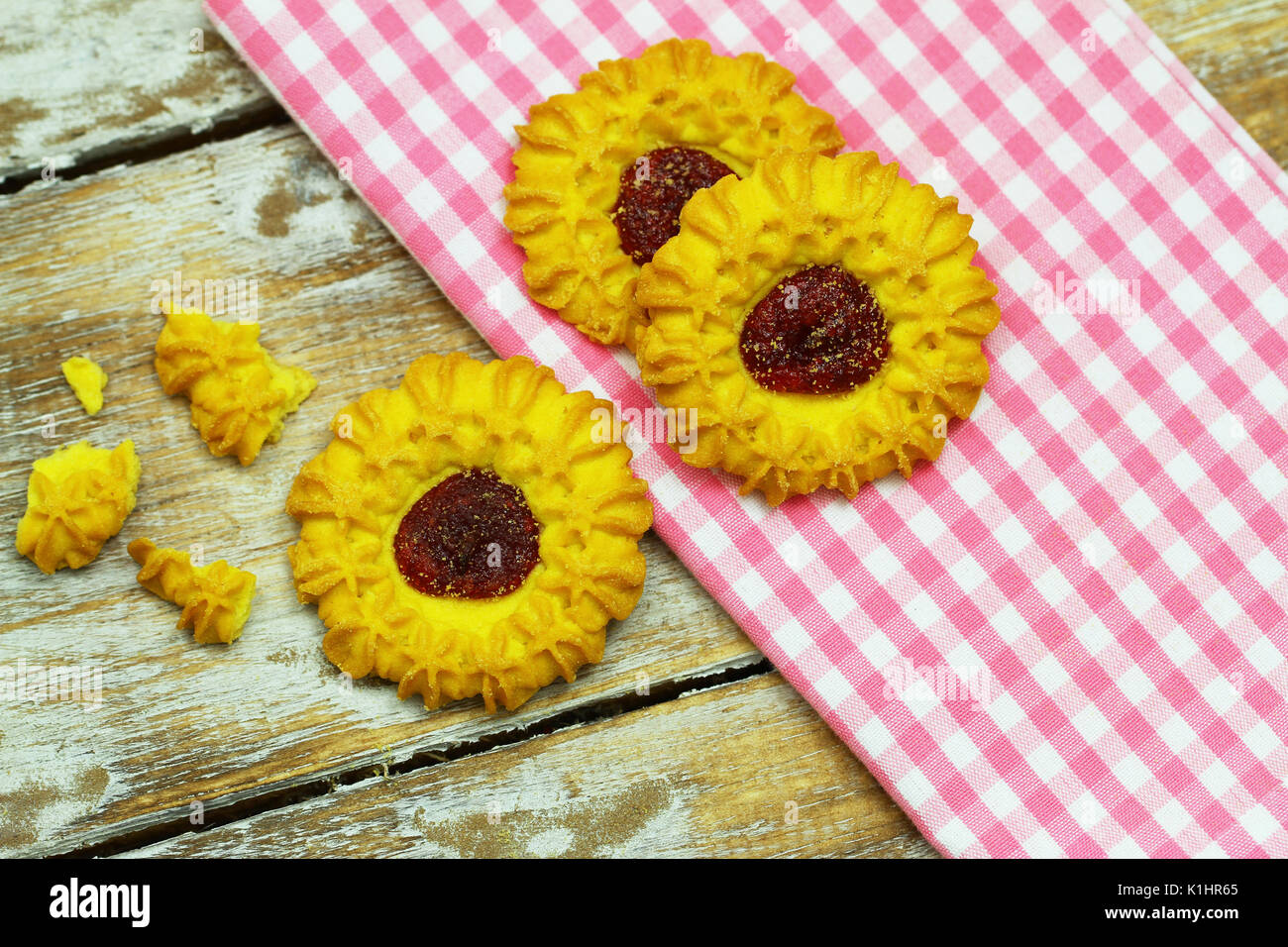 Biscotti croccanti con confettura di fragole sul panno rosa e superficie in legno Foto Stock