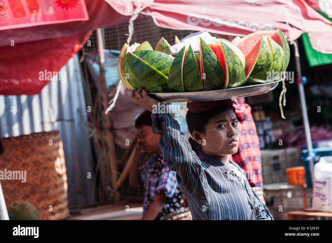 Un cocomero venditore porta un pesante vassoio caricato sulla cima della sua testa attraverso il Mercato Centrale di Mawlamyine, Stato Mon, Myanmar. Foto Stock