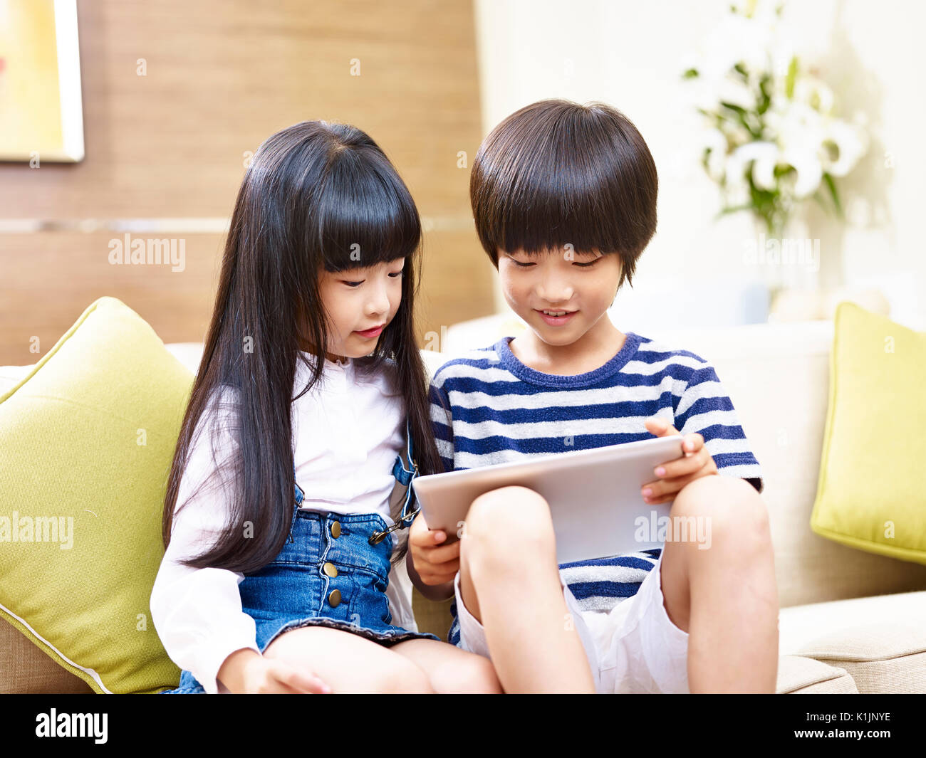 Little asian fratello e sorella seduta sul lettino usando tavoletta digitale insieme. Foto Stock